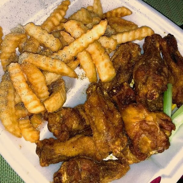 A white takeout container filled with crispy America's Best Wings and seasoned crinkle-cut fries.