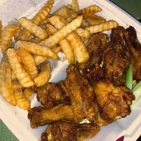 America's Best Wings Eastern Ave wings and crinkle-cut fries, seasoned with pepper, in a white takeout container.