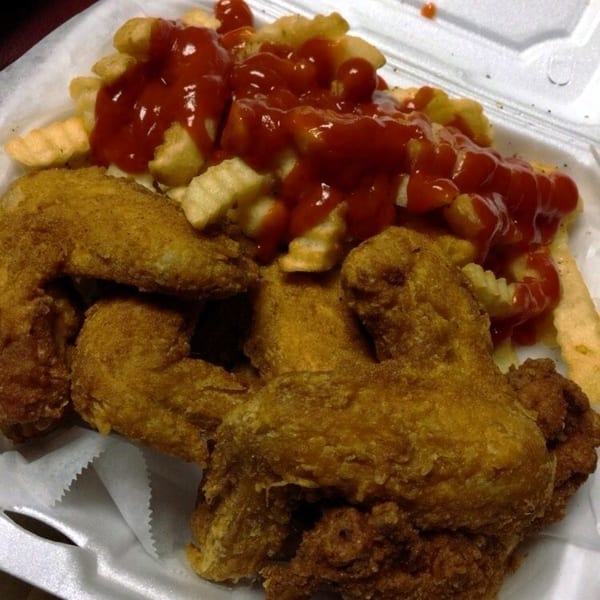 Golden-brown fried chicken wings and crinkle-cut fries with ketchup in a white takeout container.
