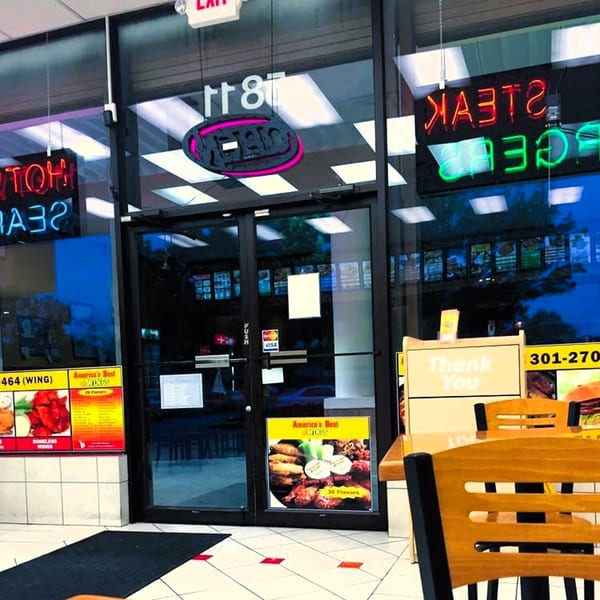 Exterior view of America's Best Wings entrance with neon signs and menu posters visible through the glass.