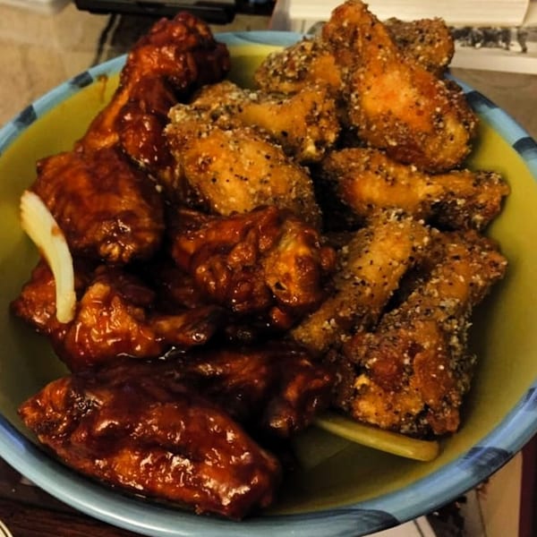 A bowl of America's Best Wings with half barbecue and half lemon pepper wings, garnished with celery.